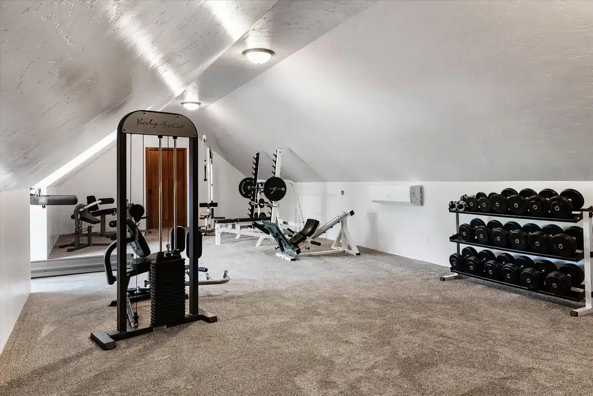 Fully equipped workout room at Mansion on the Lake with treadmill, weight bench, leg press, exercise machines, and large windows with natural light